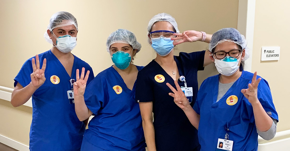 Four nurses inside hospital holding up three fingers
