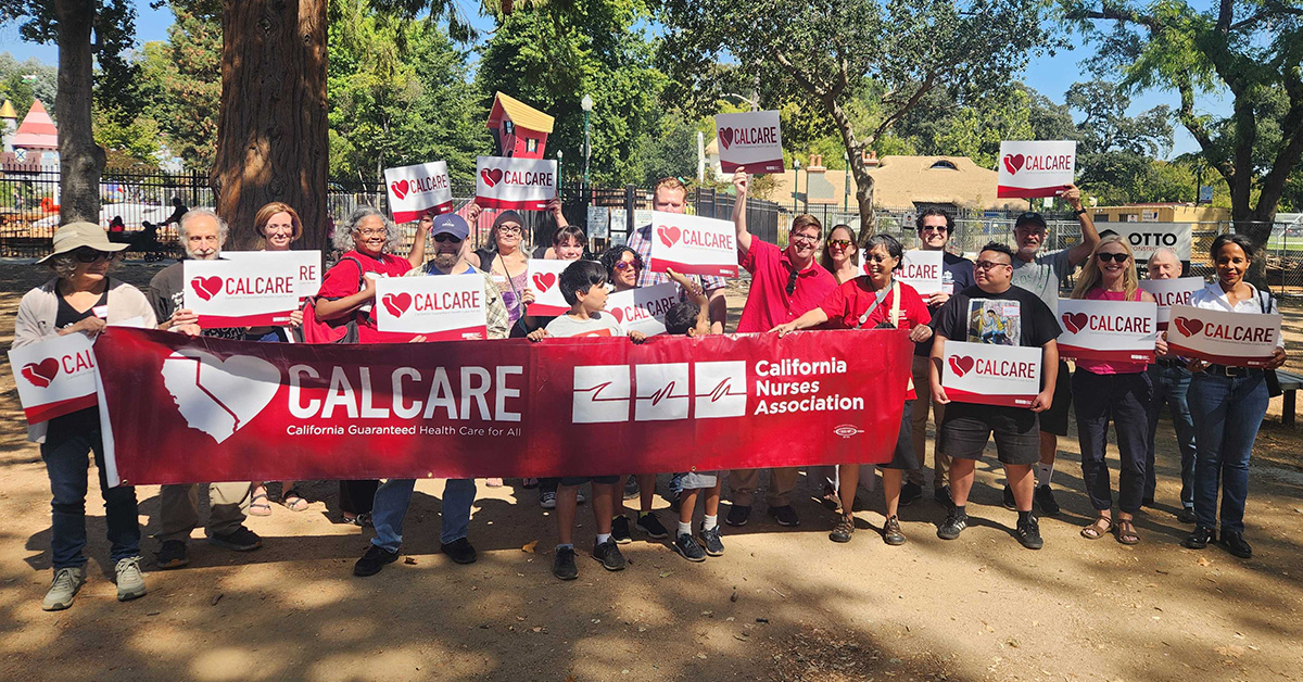 Large group of activists in park holding CalCare signs and banner